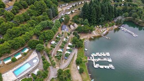 An aerial view of a lakeside property with a swimming pool, docked boats, and a variety of cabins and houses. - Camping Lac de Villefort (Pourcharesses)