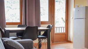 A modern living room with a sofa, dining table, chairs, and a refrigerator. - Camping Lac de Villefort (Pourcharesses)