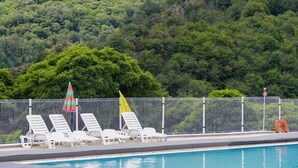 A swimming pool with white lounge chairs and a fence. - Camping Lac de Villefort (Pourcharesses)