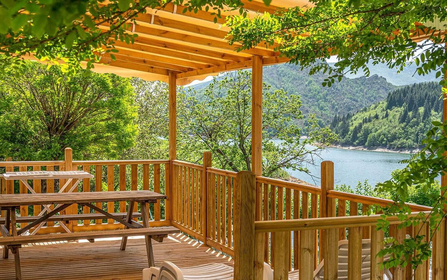 Una terraza de madera con mesas de picnic con vistas a un lago y colinas boscosas.