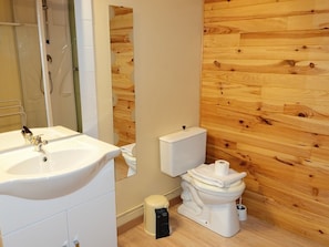 Et badeværelse med trævæg, hvid vask og toilet.