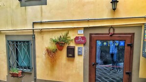 Fachada de edificio con puerta de madera, ventana con barrotes de metal y una planta en maceta en la pared.