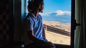 Una persona sentada junto a una ventana con vistas a un paisaje montañoso.