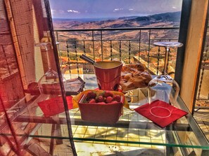 A balcony with a view of a mountainous landscape, a glass table with a red napkin, a basket of strawberries, and a chocolate bar. - B&B al centro storico (Troina)