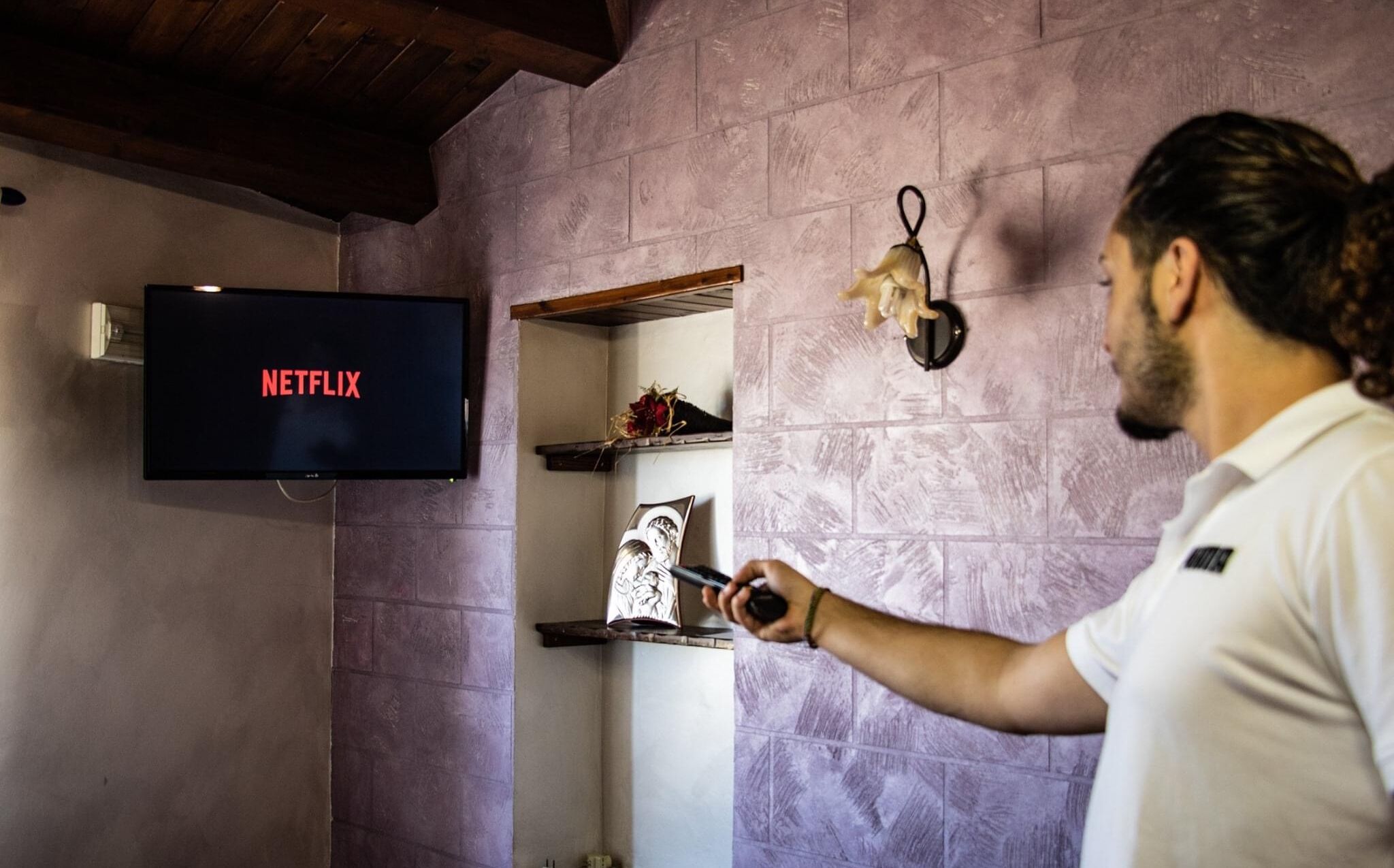 A person holding a remote control in front of a television displaying the Netflix logo.