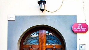 Una puerta doble de madera con arco en la parte superior, una pequeña ventana encima y un farol de calle. Se ve un cartel con el número 52 en la pared a la izquierda.