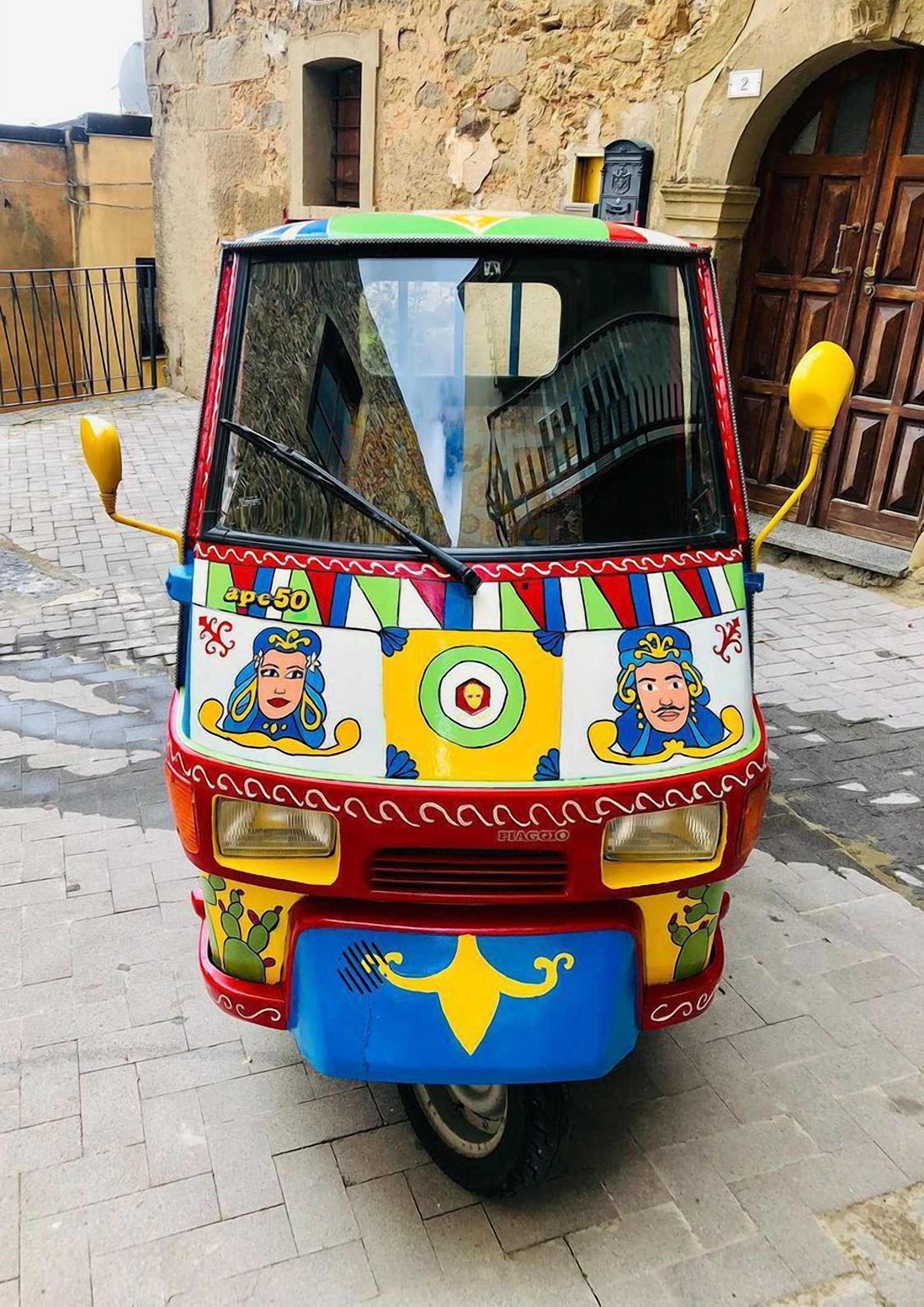 A colorful three-wheeled vehicle parked on a cobblestone street.