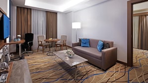 Habitación de hotel con sofá, dos sillones, una mesa de centro, televisor y lámpara.
