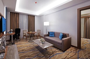 A hotel room with a sofa, two chairs, a coffee table, a TV, and a lamp.