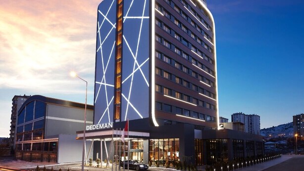 Un hotel moderno con un llamativo letrero de 'DEDEMAN', que presenta una fachada geométrica y una entrada amplia.