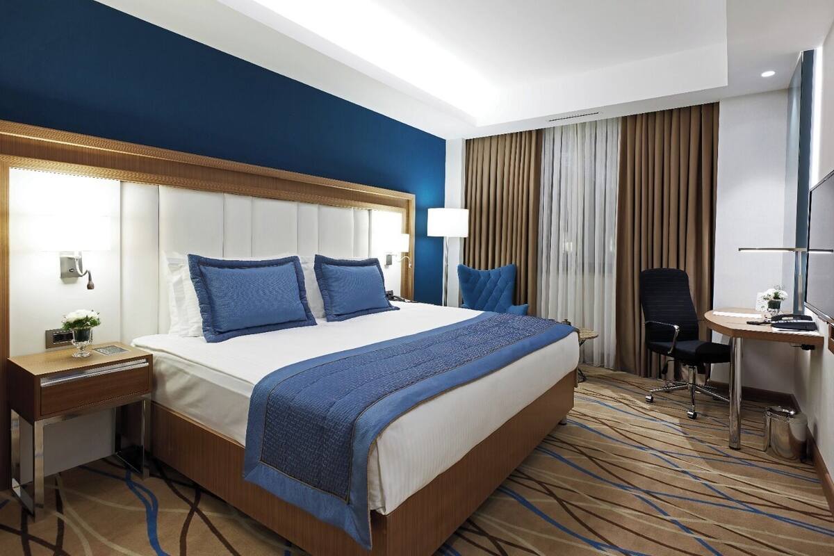Habitación de hotel con una cama grande, un escritorio, una silla y un televisor.