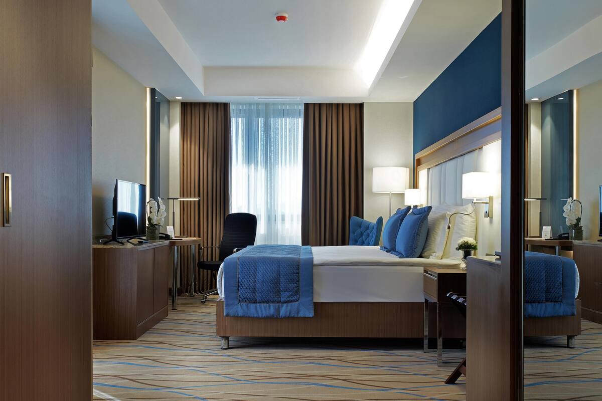 Una habitación de hotel moderna con una cama grande, un escritorio, una silla y un espejo.