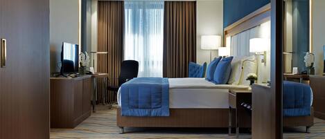 A modern hotel room with a large bed, a desk, a chair, and a mirror.