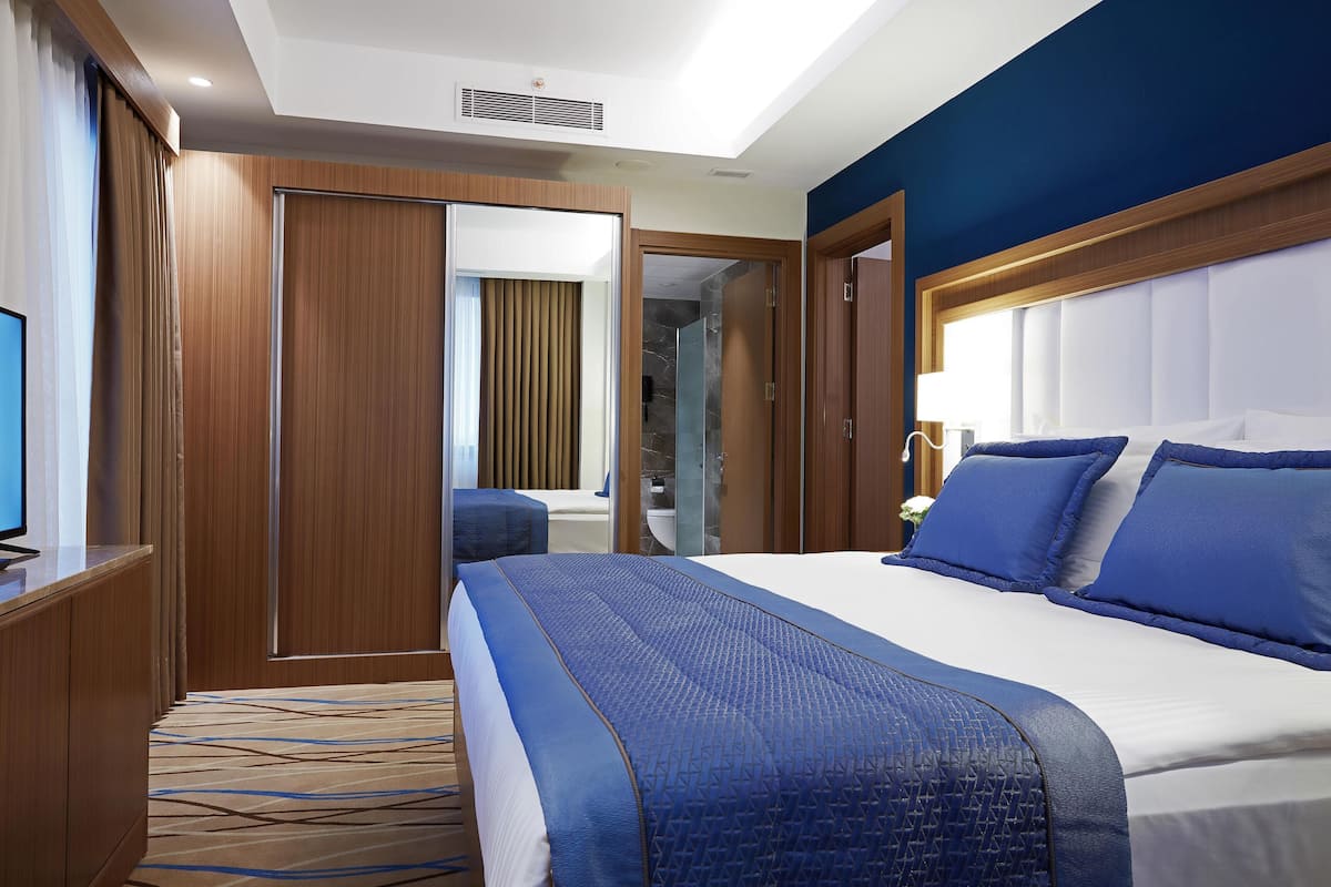 Habitación de hotel con una cama grande, televisión, escritorio y baño visible a través de una puerta abierta.