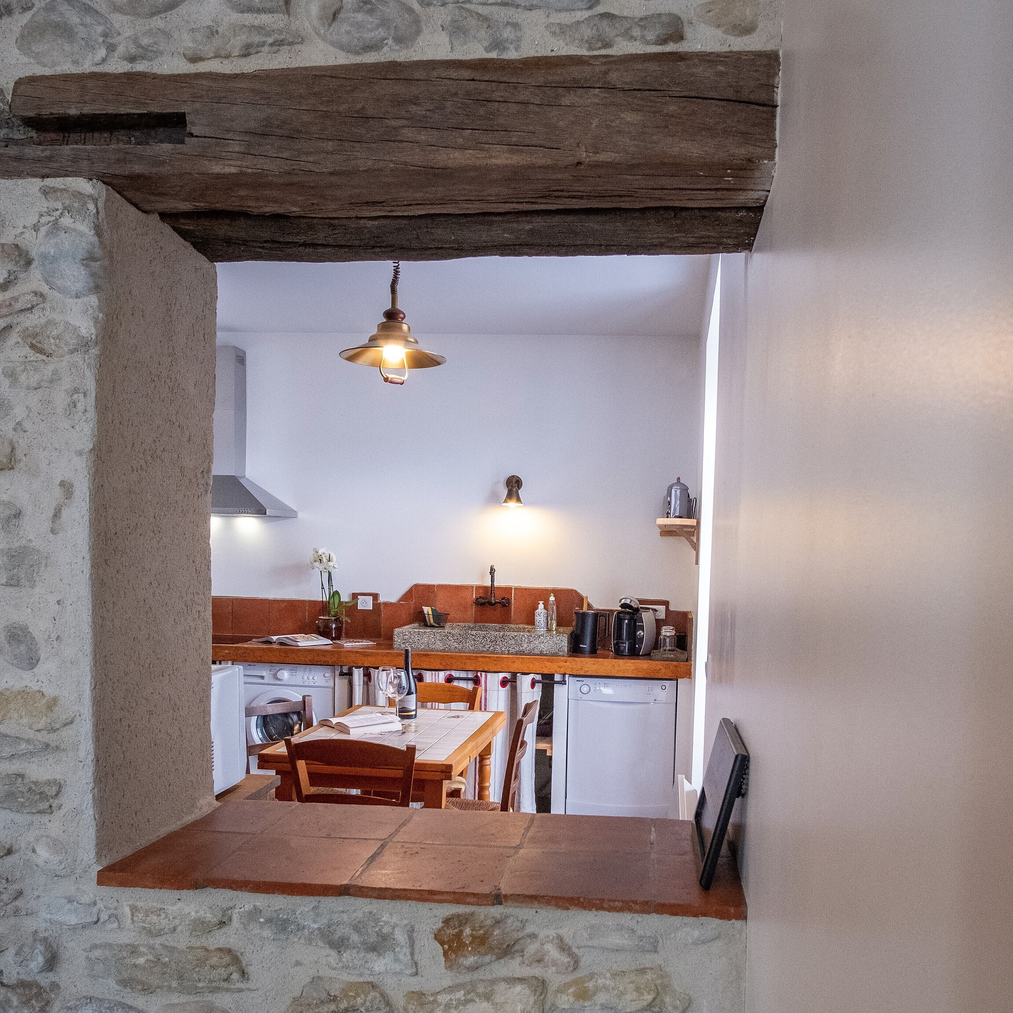 Una cucina rustica con parete in pietra, travi in legno, lampadario a sospensione, tavolo da pranzo e lavatrice.