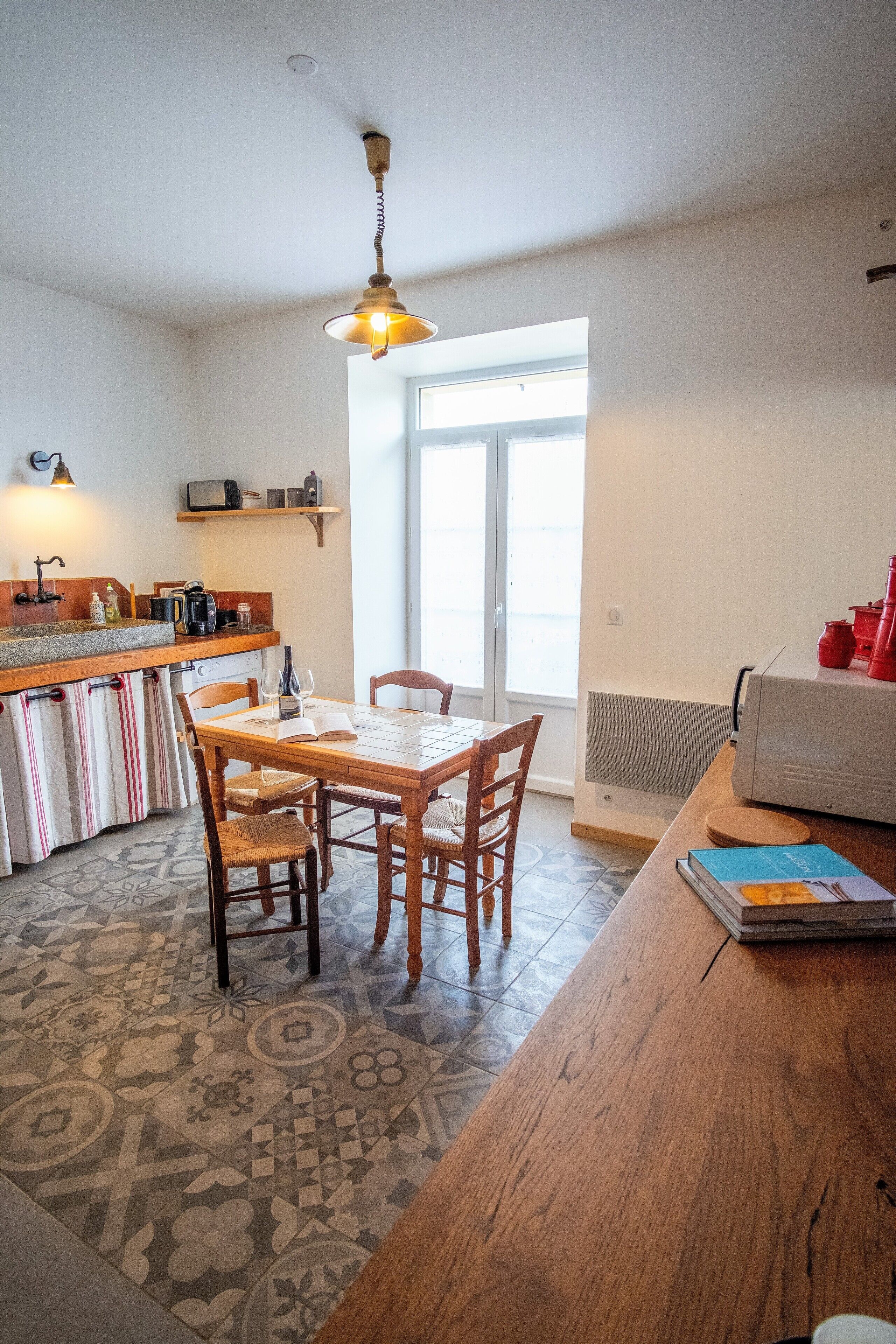 A kitchen with a wooden table and chairs, a hanging light fixture, and a window with a view.