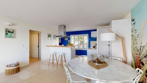 A modern kitchen with a blue accent wall, a dining area with a marble table, and a view through the window. - Magnificent waterfront apartment (Grand-Case)
