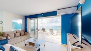 A modern living room with a sofa, coffee table, and a view of the sea through large sliding doors. - Magnificent waterfront apartment (Grand-Case)