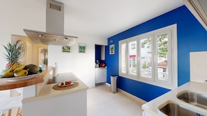 A kitchen with a blue accent wall, white cabinets, a stainless steel sink, and a fruit bowl on the counter.