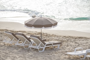 A beach with white lounge chairs and a brown umbrella.