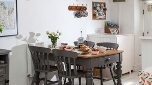 A dining area with a wooden table, chairs, and a coffee pot. There is a map on the wall and a coat rack with a jacket.