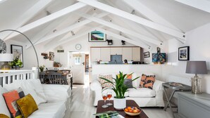 A spacious living room with a high ceiling, white walls, and a kitchen area.