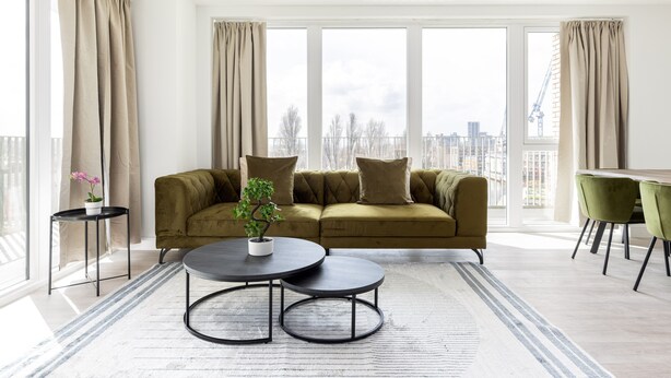 A modern living room with a sofa, two round tables, and a potted plant. - The Wembley Apartment (Wembley)