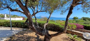Un espace extérieur bordé d’arbres, offrant une vue sur la mer et les montagnes lointaines.