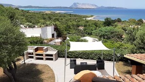 A patio with outdoor furniture, a white umbrella, and a view of the sea and mountains.