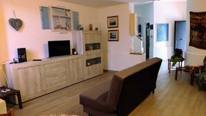 A living room with a sofa, a TV, a cabinet with glass doors, and a wall with framed pictures.