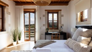 A bedroom with a bed, bedside table, desk, chair, and a view of the outdoors.