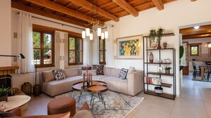 A spacious living room with a wooden ceiling, a large sofa, a coffee table, and a bookshelf.