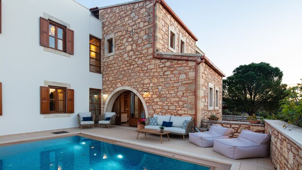 A stone building with a pool, outdoor seating, and a large tree.