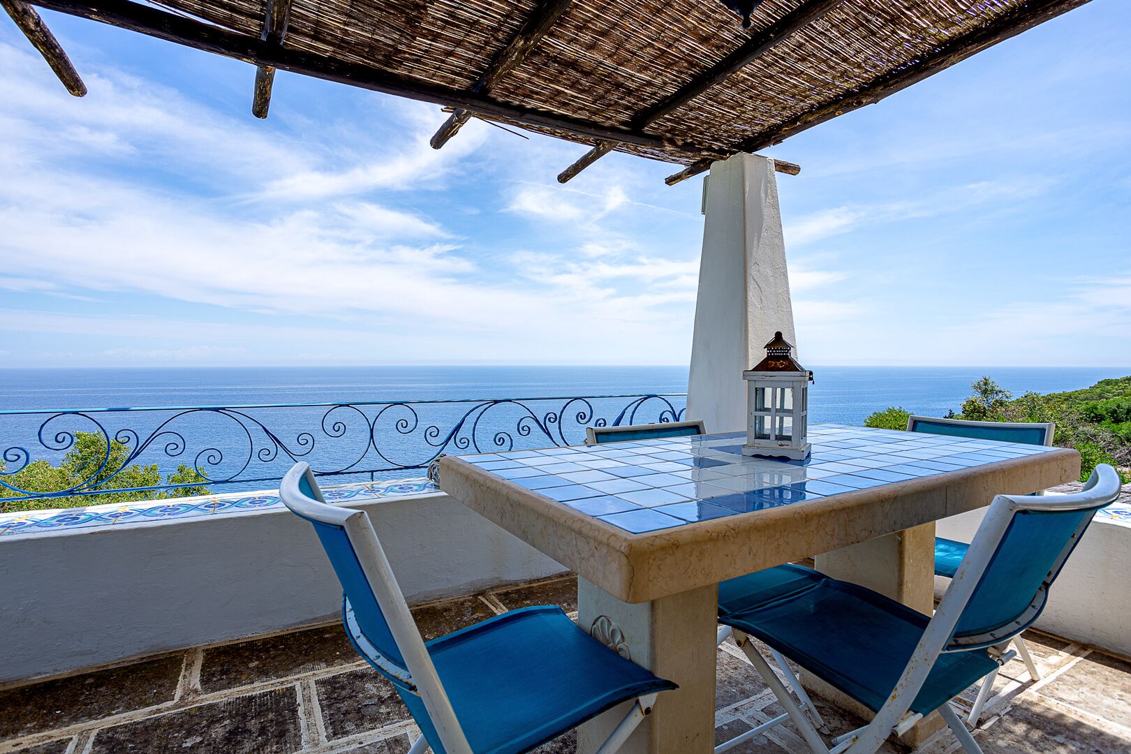 A terrace with a table and chairs, a lantern, and a view of the sea.