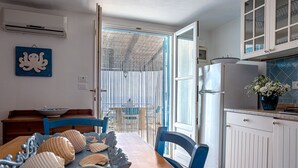 Eine Küche mit einem Holztisch, Stühlen, einem Kühlschrank und einem Fenster mit Blick auf einen Balkon.
