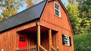 Een houten chalet met een rode deur, een balkon en een metalen dak.