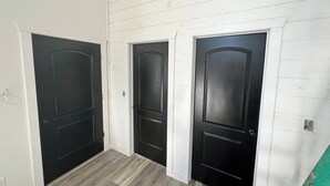 Een hal met drie zwarte deuren, witte muren en een houten vloer.