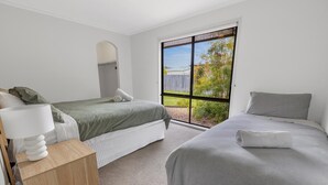 Un dormitorio con dos camas, una mesita de noche de madera, una lámpara y un amplio ventanal que ofrece vistas al exterior.