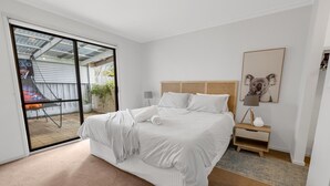 Un dormitorio con cama, mesita de noche, lámpara, un cuadro enmarcado y una puerta corrediza de vidrio que da a un espacio exterior.