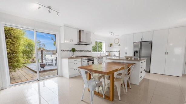 Una cocina moderna con armarios blancos, una mesa de comedor de madera y un ventanal con vistas a un jardín.