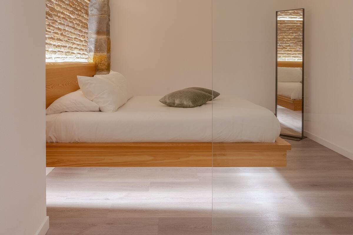 A bedroom with a wooden bed, white bedding, and a brick wall.
