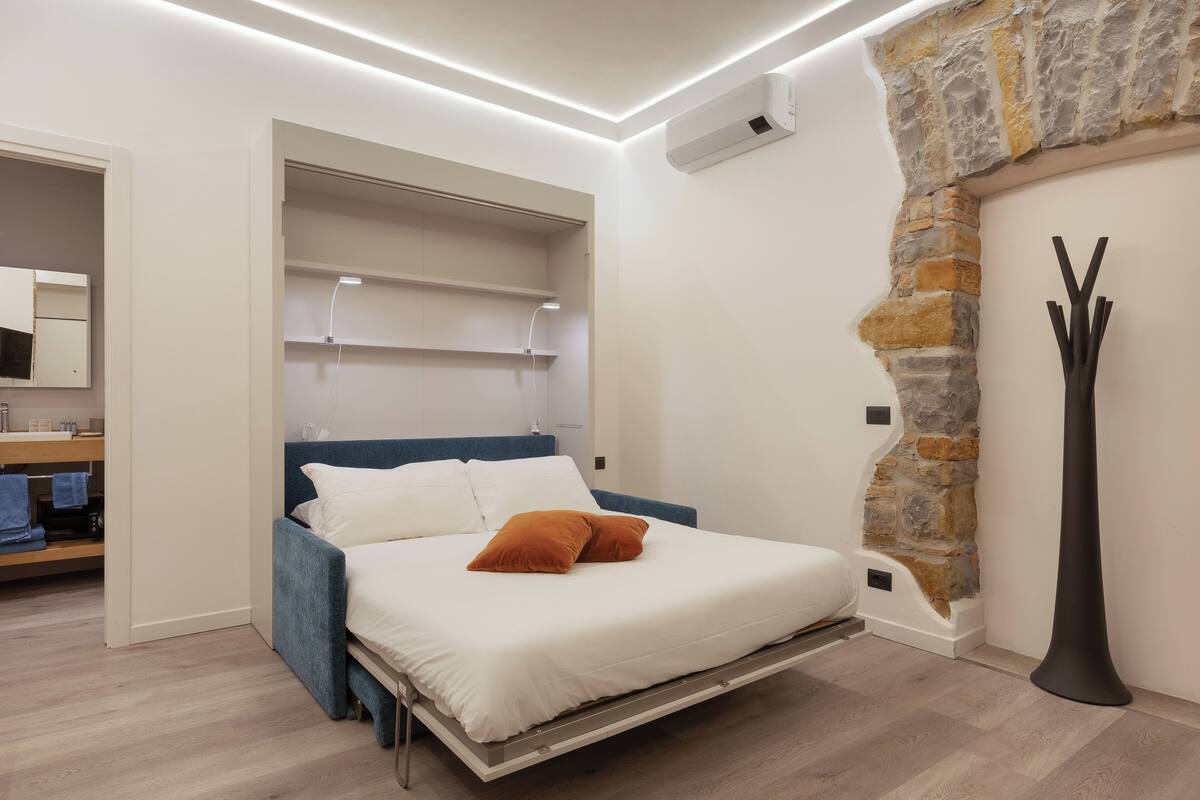 A modern bedroom with a bed, built-in shelving, a stone accent wall, and a tall floor lamp.