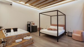 Un dormitorio moderno con una cama con dosel, una bañera integrada y un área de descanso con un sillón acolchado.
