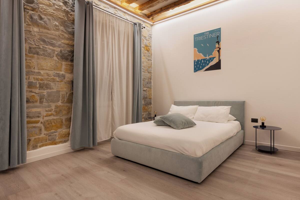 A bedroom with a stone wall, a bed with grey bedding, and a small round table with a globe.