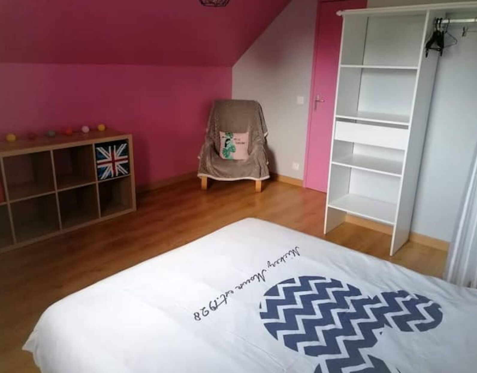 A bedroom with a bed, a wardrobe, a chair, and a shelf with toys.