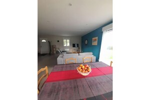 Un coin repas avec une table dressée pour deux personnes, un panier de fruits et un canapé en arrière-plan.