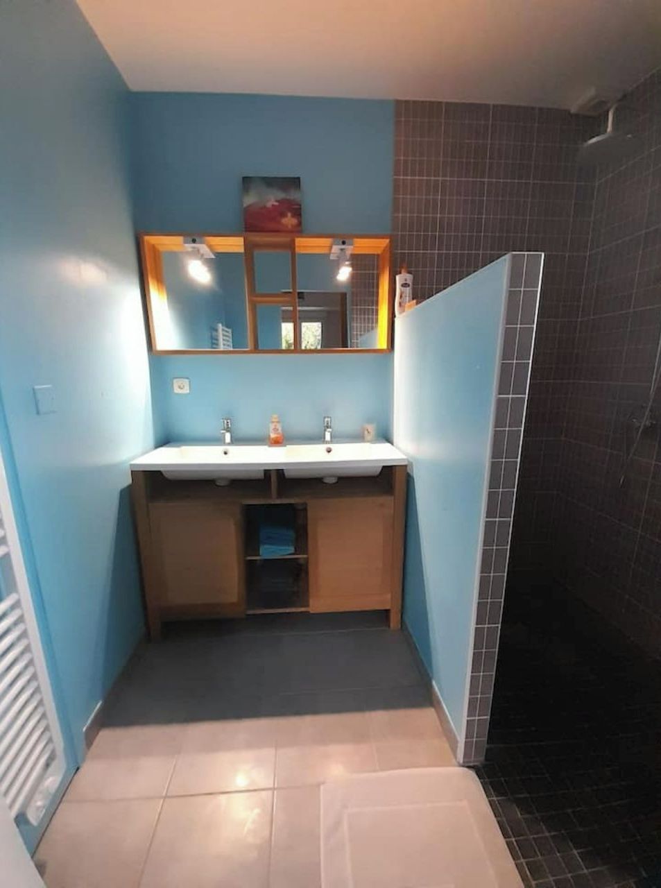 A bathroom with a blue wall, a white sink, a mirror, and a tiled shower area.