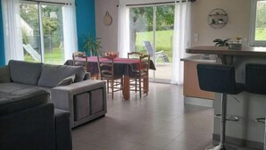 A modern living room with a sofa, a dining table with chairs, and a kitchen area with a bar. - forest house (Le Theil-en-Auge)