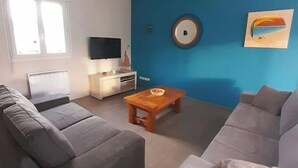 A modern living room with two grey sofas, a wooden coffee table, a flat-screen TV, and a blue accent wall. - forest house (Le Theil-en-Auge)