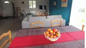 A dining area with a table set for two, a basket of fruit, and a sofa in the background. - forest house (Le Theil-en-Auge)